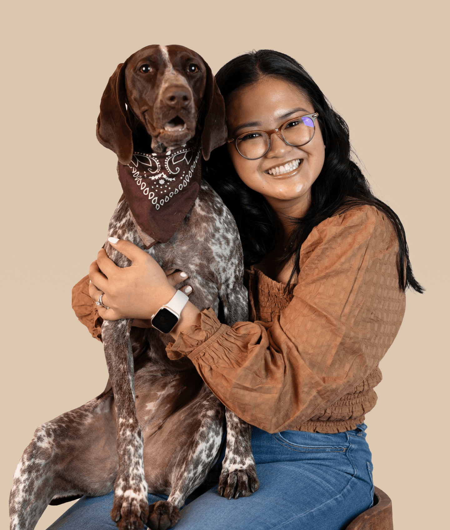 A brown dog named Sage wearing a brown bandanna on their neck with a human companion looks at the camera